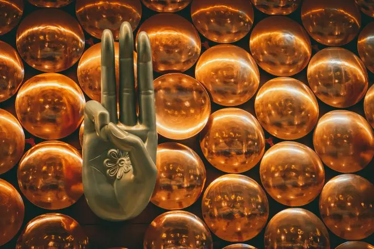 A bronze human hand in a mudras pose, background of golden orbs